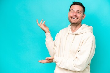 Wall Mural - Young caucasian handsome man isolated on blue background extending hands to the side for inviting to come