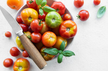 Freshly harvested tomatoes and herbs arranged in a bowl with a knife on a bright kitchen countertop