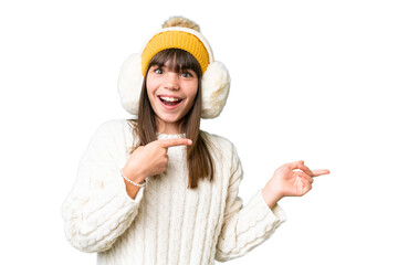 Sticker - Little caucasian girl wearing winter muffs over isolated background surprised and pointing side