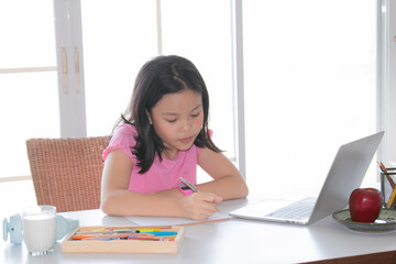 Adorable Asian girl happy learning online with technology laptop on desk at home, school girl typing answer or response with teacher study homeschool or learn from home, smart kids with technology