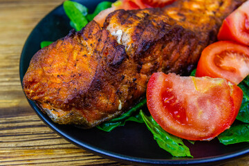 Plate with roasted salmon steak, tomatoes and spinach leaves on a wooden table