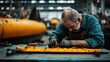 © svastix - A focused man assembles mechanical components on a workbench in an industrial facility surrounded by yellow machinery, demonstrating precision engineering and craftsmanship.
