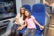 © mitarart - Smiling girls seated on modern train, experiencing travel comfort and joy during their vacation adventure