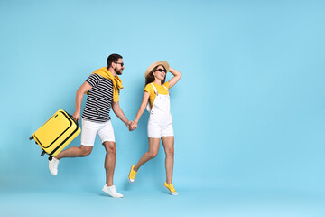 Poster - Happy couple with suitcase running on light blue background