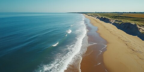 A stunning aerial view of a pristine beach with golden sand, gently rolling waves, and clear blue water on a serene sunny day, ideal for relaxation