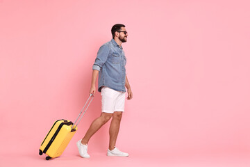 Wall Mural - Happy man in sunglasses with suitcase on pink background