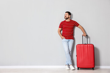 Canvas Print - Happy man with suitcase near light gray wall indoors, space for text