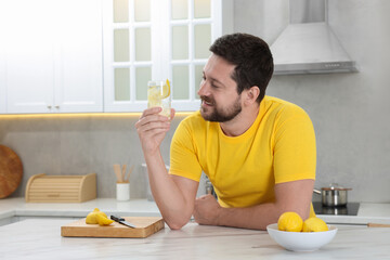 Wall Mural - Happy man holding glass of water with lemon in kitchen