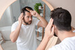 © New Africa - Man brushing his hair near mirror indoors. Alopecia problem
