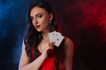 Canvas Print - Poker game. Charming woman with playing cards on black background in color lights and smoke