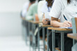 © EduLife Photos - Students Taking Exam in Classroom Setting. Students in uniforms are seated in a classroom, writing answers during an exam, highlighting focus and academic testing.