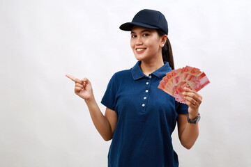 Young hispanic woman courier wearing delivery uniform and cap holding indonesia money rupiah smiling happy pointing with hand and finger to the side