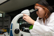 © kwanchaichaiudom - Cute scientist schoolgirl in lab coat looks through microscope for study microbiology in laboratory.