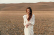 © SHOTPRIME STUDIO - Woman standing in white dress in open field with mountains in background on travel beauty and fashion photoshoot