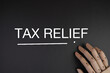 © Ardini - handwritten of TAX RELIEF on black background with wooden hand.