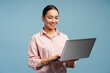© Maria Vitkovska - Attractive smiling professional Asian woman smiling and typing on laptop isolated on blue background