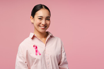 Smiling asian woman smiling wearing pink ribbon showing support for breast cancer awareness