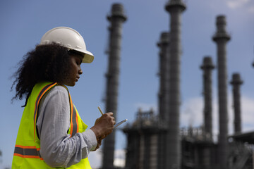 Black female technician taking notes while using a digital tablet at a thermal power plant.