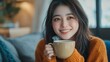 © The Little Hut - Joyful young asian female enjoying a cup of coffee while sitting on the rug beside to the sofa at home Cosy scene Smiling pretty woman drinking hot tea : Generative AI