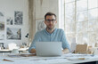 © Ailish_ART - A professional photo of a man sitting at his desk in front of a laptop, wearing a shirt.