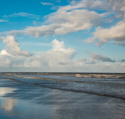 A beautiful lonely sea beach with blue sky and scattered clouds reflect on the sea water at the dusk.