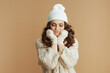 © Alliance - sad elegant woman in beige sweater, mittens and hat on beige