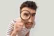 © Pixel-Shot - Young man looking through magnifier on light background, closeup