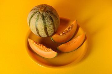 Plate with tasty ripe melon and cut slices on orange background