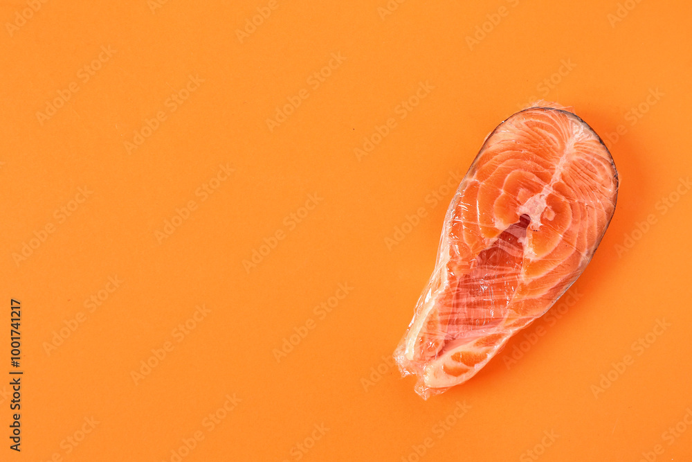 Fresh salmon steak in plastic food wrap on orange background