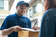 © Patcharanan - Delivery man holding a cardboard box while woman putting signature in clipboard. Hand female accepting a delivery boxes of paper containers from delivery man. Signing to get package. Delivery concept.