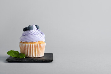 Wall Mural - board of tasty cupcake with blueberries on grey background