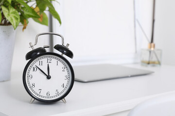 White desk with alarm clock, laptop and houseplant, closeup