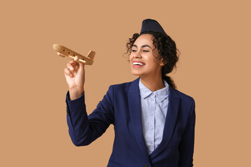 Wall Mural - Beautiful African-American stewardess with toy plane on beige background