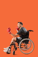 Poster - Sporty young man in wheelchair with boxing gloves on orange background