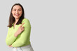 © Pixel-Shot - Smiling young woman pointing at something on grey background
