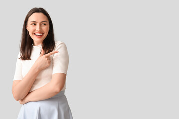 Wall Mural - Smiling young woman pointing at something on grey background