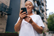 © dikushin - Low-angle view of gray-haired senior lady using smartphone texting message standing on urban street on summertime. Middle aged woman grandma hold phone typing sms enjoying communication in mobile app.