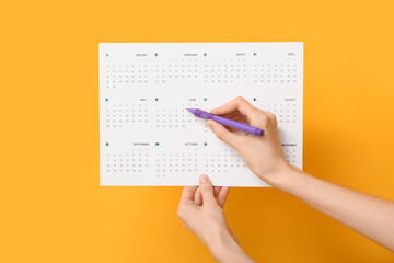 Female hands marking date in calendar on yellow background