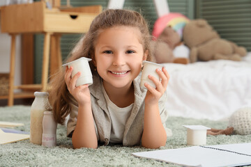 Wall Mural - Happy little girl with yogurt packs lying on floor in room