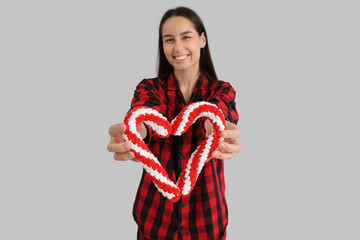 Sticker - Happy young woman in pajamas with Christmas candy cane toys on grey background