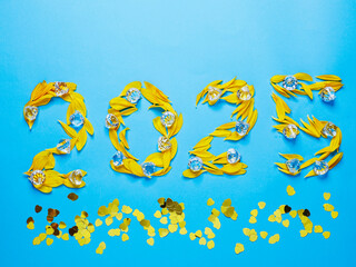 Sign 2025 made of yellow flower petals and gem stones on blue background with glamourous gold heart shaped confetti. Hand made organic numbers. Copy space on top. Love and romance concept.