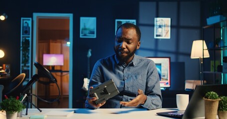 Wall Mural - BIPOC content creator filming technology review of newly launched V mount battery, unpacking it and presenting specifications to audience. Internet star showing charging device to viewership