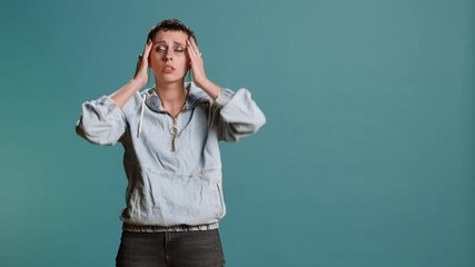 Wall Mural - Unwell model suffering from a painful headache in studio, rubbing her temples and being frustrated about discomfort. Young stylish woman with a migraine feeling displeased and worried. Camera B.