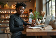 © Derek Brumby - A young woman with natural hair works intently on her laptop in a cozy cafe, surrounded by plants and pottery, creating a peaceful and focused atmosphere.