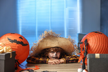 Wall Mural - Cute boy dressed like scarecrow with festive decor and gift boxes indoors at night. Halloween celebration