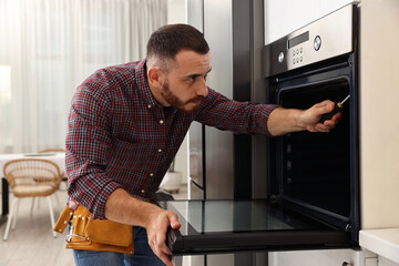 Canvas Print - Repairman with screwdriver fixing oven at home