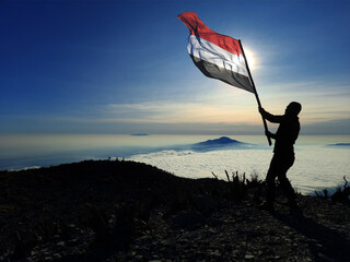 man raising the flag of yemen on the top of the mountain. background of mountains at sunset or sunrise. yemen flag for Independence Day.