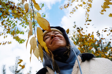 Woman in autumn attire smiling under yellow leaves on sunny day. Enjoying fall outdoors concept.