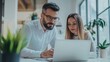 © Luxetify - A bearded man and a woman are looking at a laptop computer in an office.