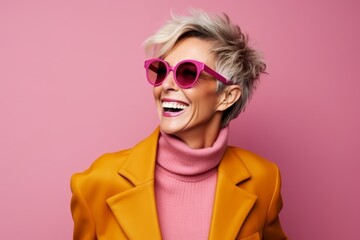 Wall Mural - Fashionable woman in yellow coat and pink sunglasses on pink background